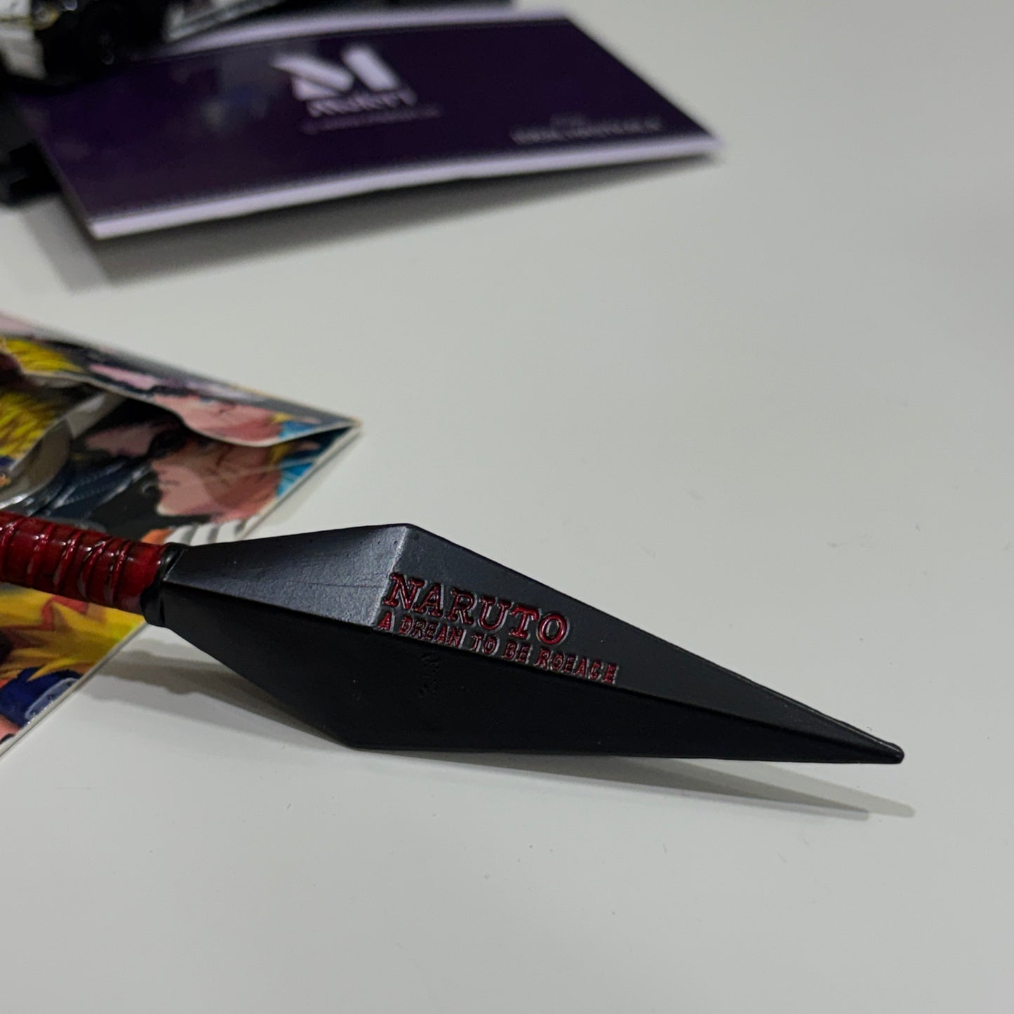 Black kunai with red handle on a white surface, featuring 'Naruto' branding.